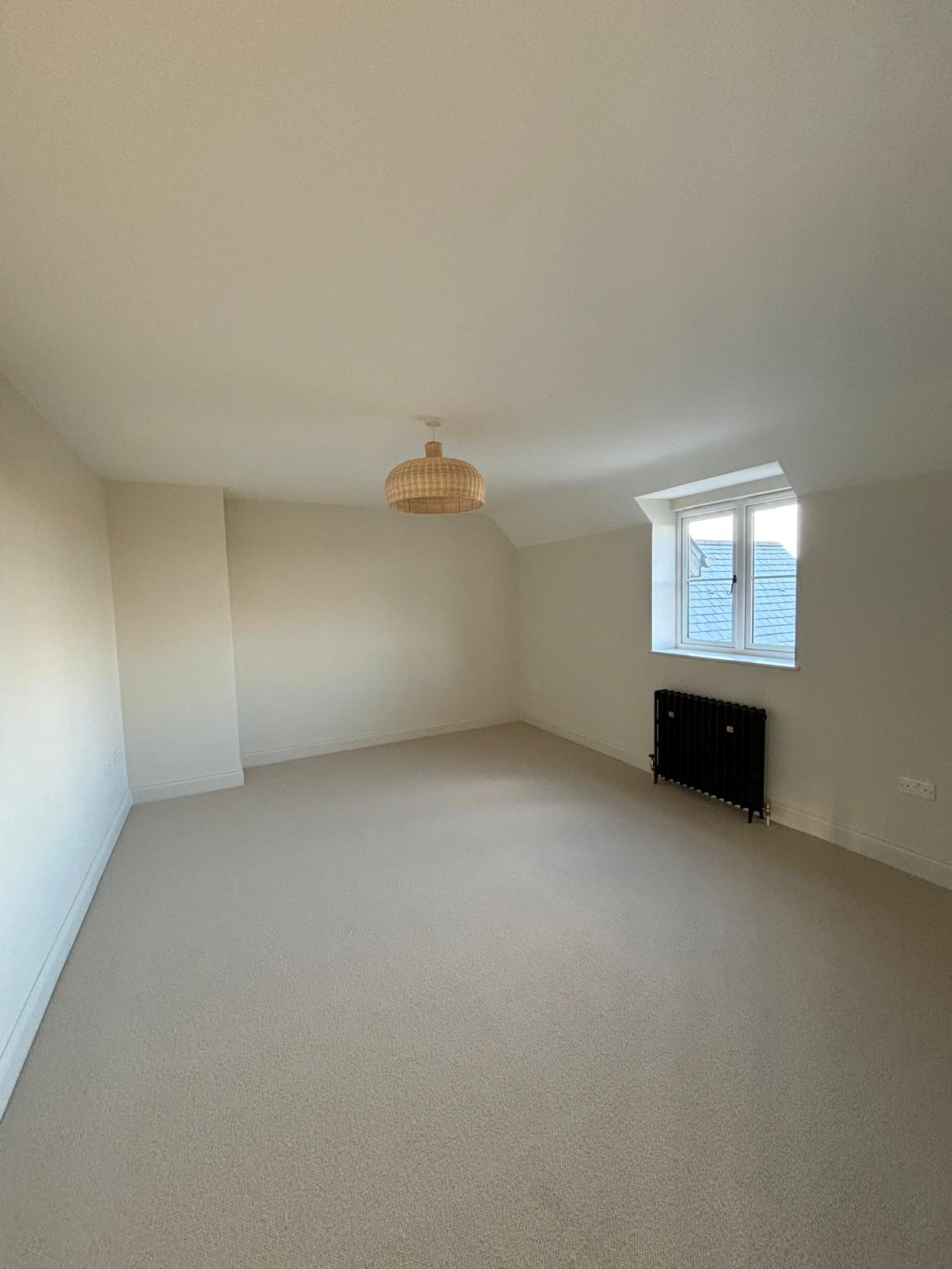 Empty carpeted bedroom with wicker pendant light after builder's clean